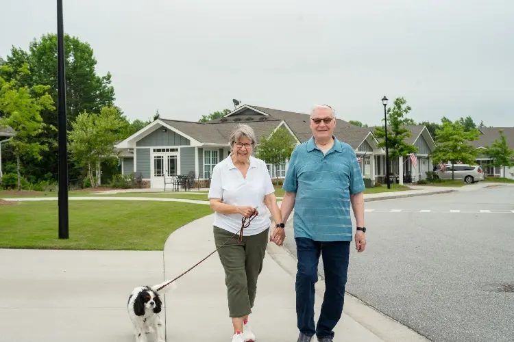 Two Horizon residents walking a dog past the cottages